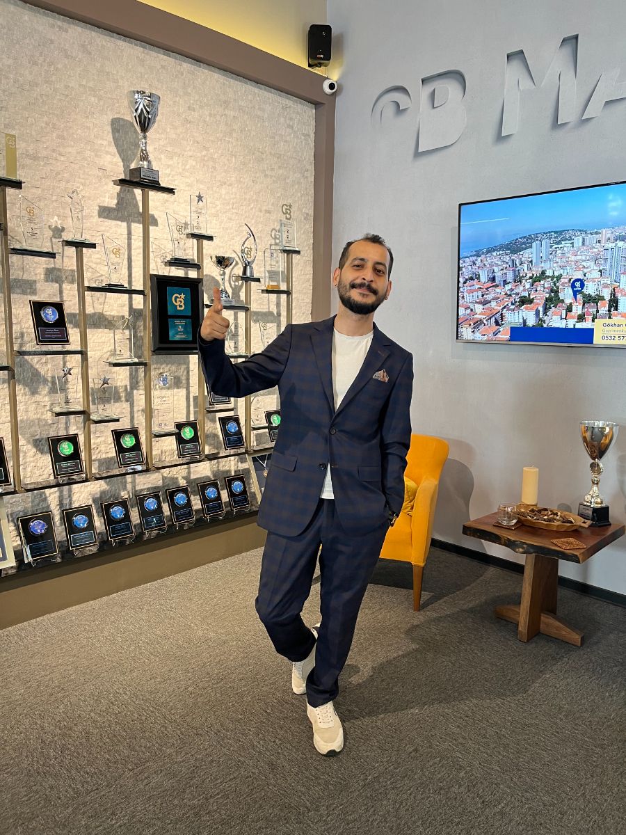 Sertan Dede — Coldwell Banker ödül duvarı önünde
